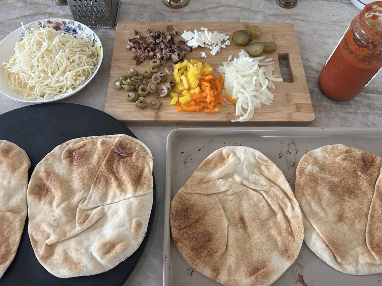 Alt Text: Ingredients for pita pizza laid out on a counter: pita bread, tomato sauce, shredded mozzarella, and fresh basil.