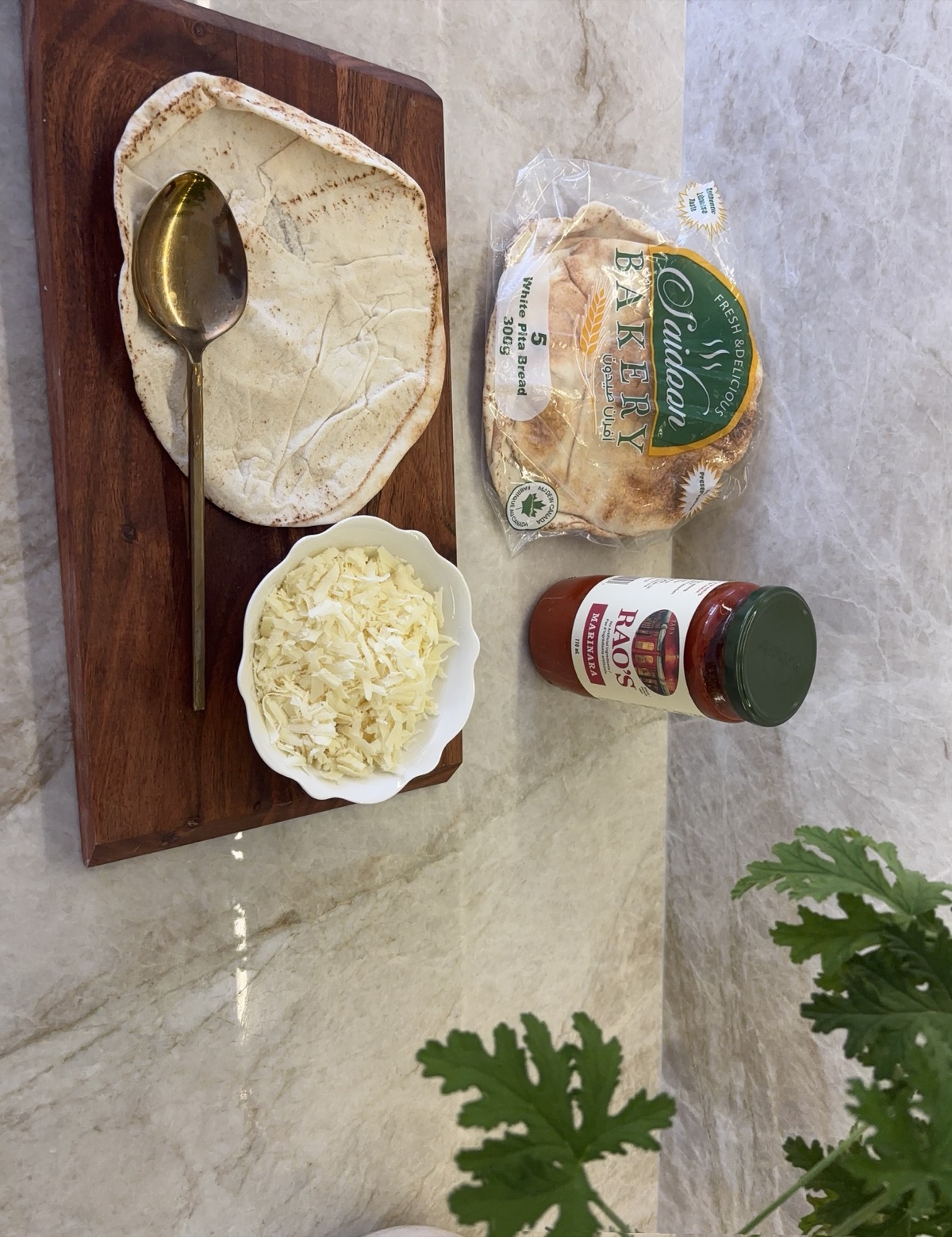 Alt Text: Ingredients for pita pizza laid out on a counter: pita bread, tomato sauce, shredded mozzarella, and fresh basil.